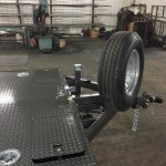 Flatbed trailer with a mounted spare tire in a workshop with various tools and equipment in the background.