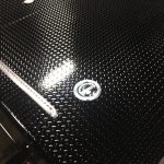 Close-up of a black diamond plate metal surface with a circular metal emblem and a reflective strip.