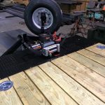 A mounted winch and spare tire on a metal frame with wooden planks, likely part of a trailer in a workshop.
