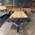 Flatbed utility trailer with wooden deck parked inside a garage or workshop with tools visible in the background.
